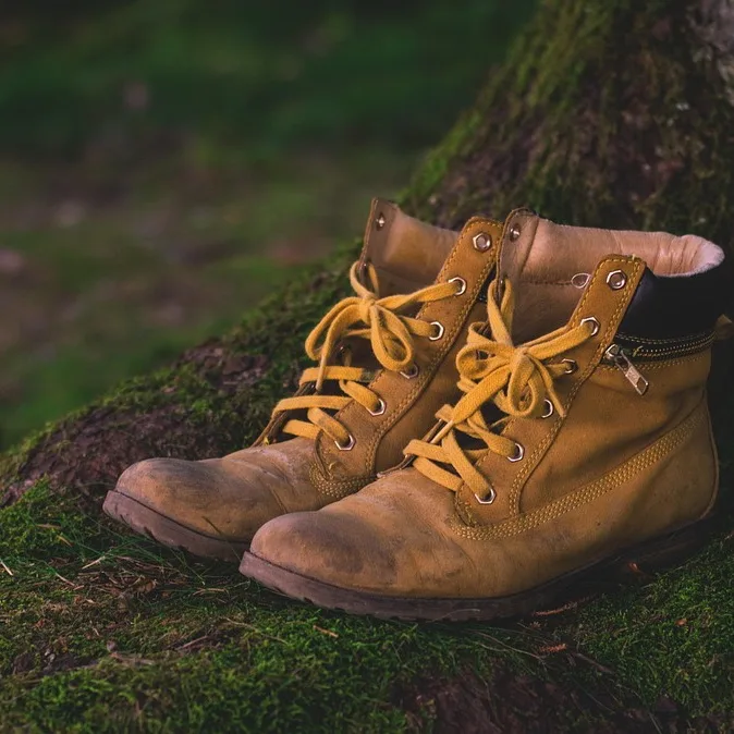 A pair of worn leather hiking boots, laces undone, resting on moss.